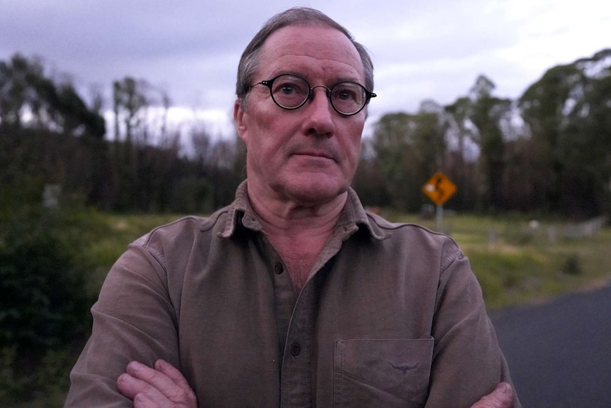 A man with glasses stands in the evening landscape.