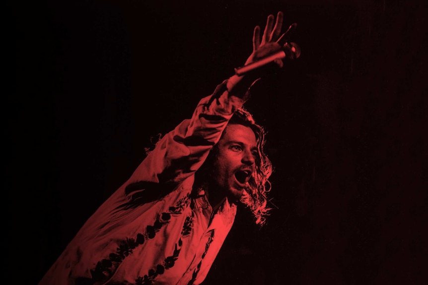 Michael Hutchence holds a microphone to the crowd during a performance.