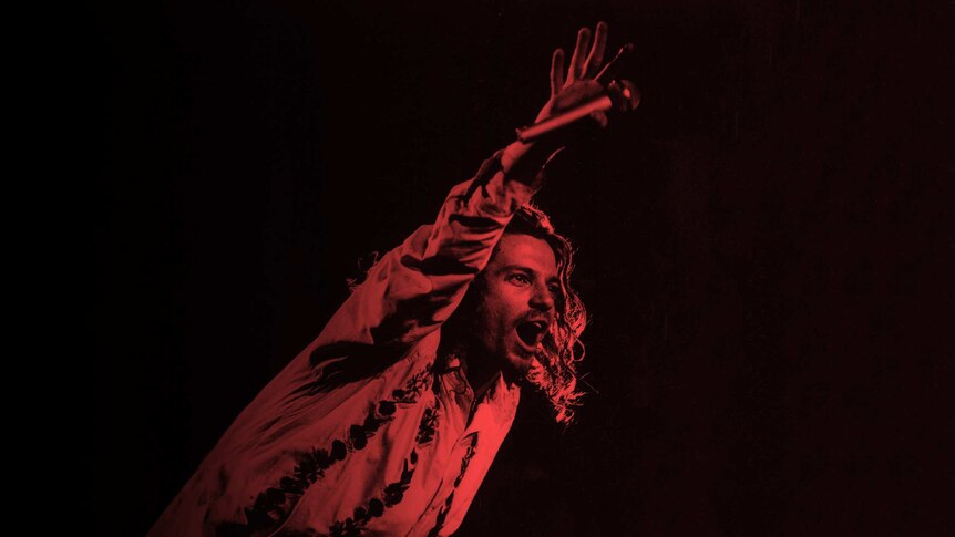 Michael Hutchence holds a microphone to the crowd during a performance.