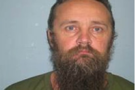 A prison mugshot of a man with a long beard.