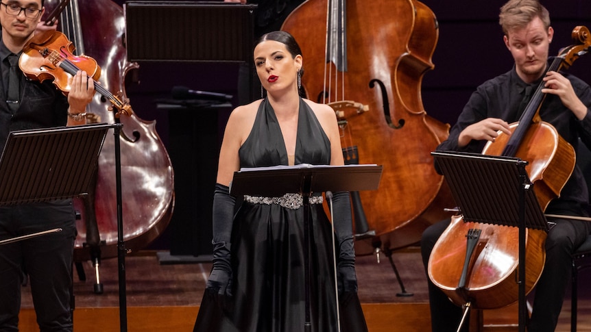 soprano wearing black gloves and dress standing in front of orchestra