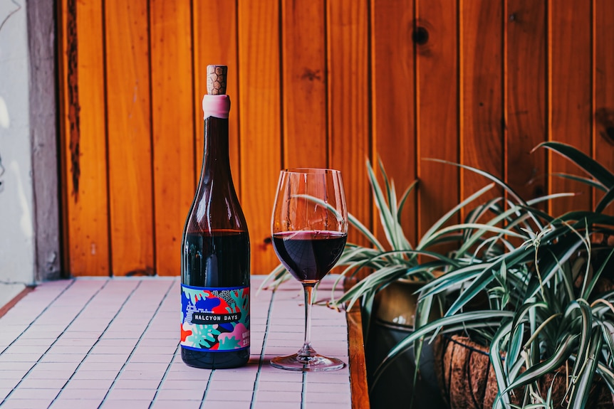 A bottle of red wine with a colourful label and a cork sticking out.