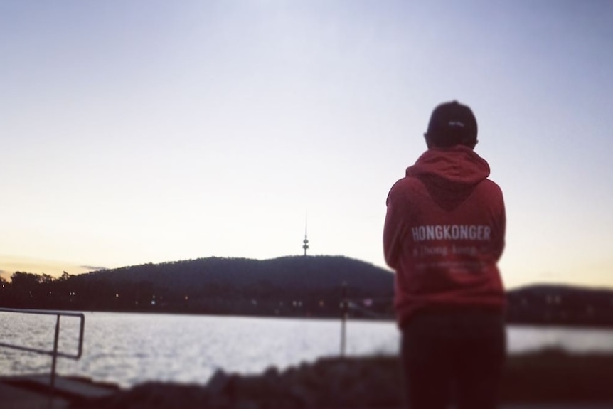 Claudia Ng wears a hoodie reading "Hongkonger" while standing in front of Lake Burley Griffin in Canberra.