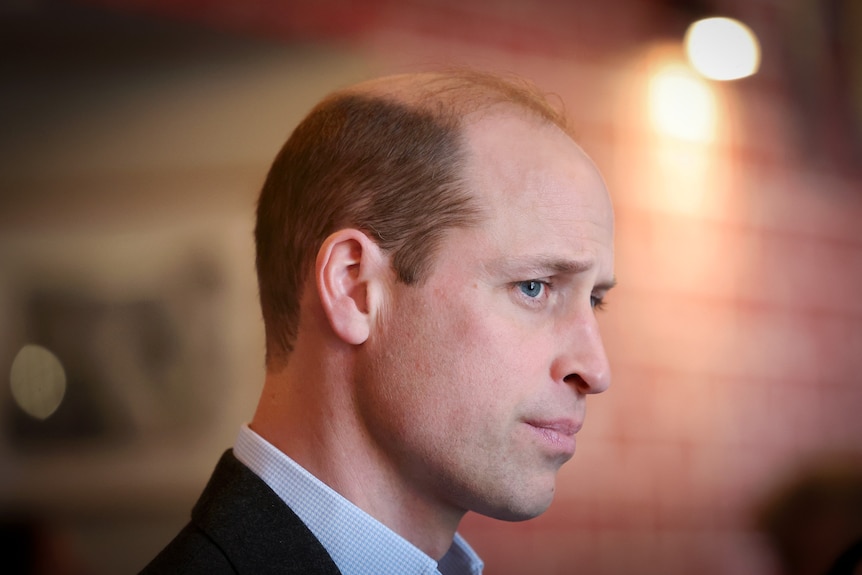 A close up of Prince William standing under a spotlight.