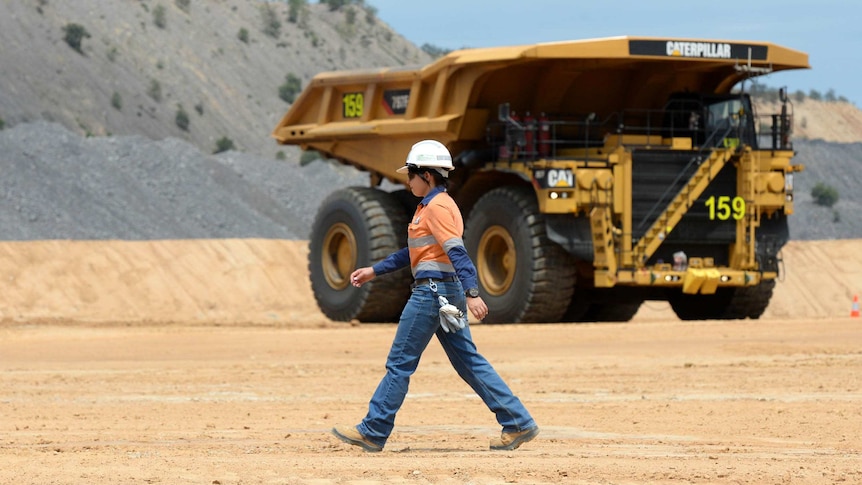 A female mine worker walks past a mine dump truck at a minesite