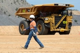 A female mine worker walks past a mine dump truck at a minesite