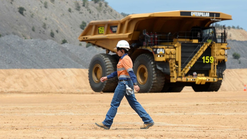 A woman walks past a dump truck at a large mining site.