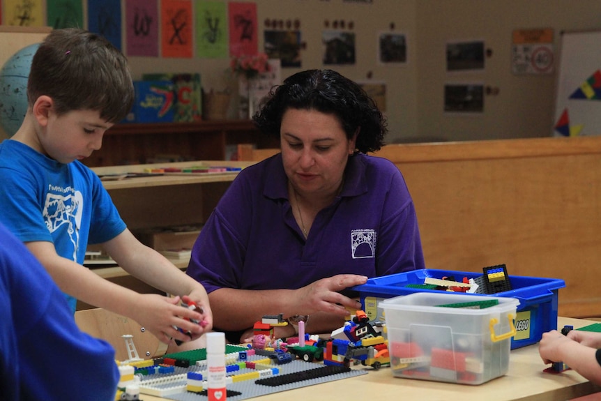 Louisa Foxford sits at a small table and plays with a child at Mountain Community Children's Centre