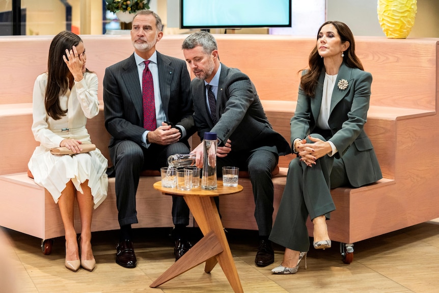 Princess Mary sits apart from Prince Frederik, legs crossed and chin upward, on a couch with two others