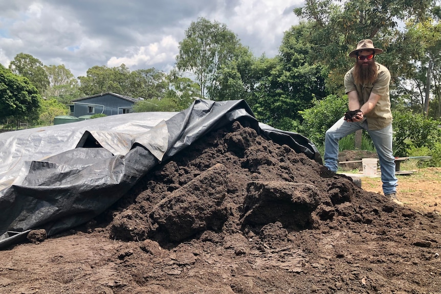A man stands next to a large pile of compost 