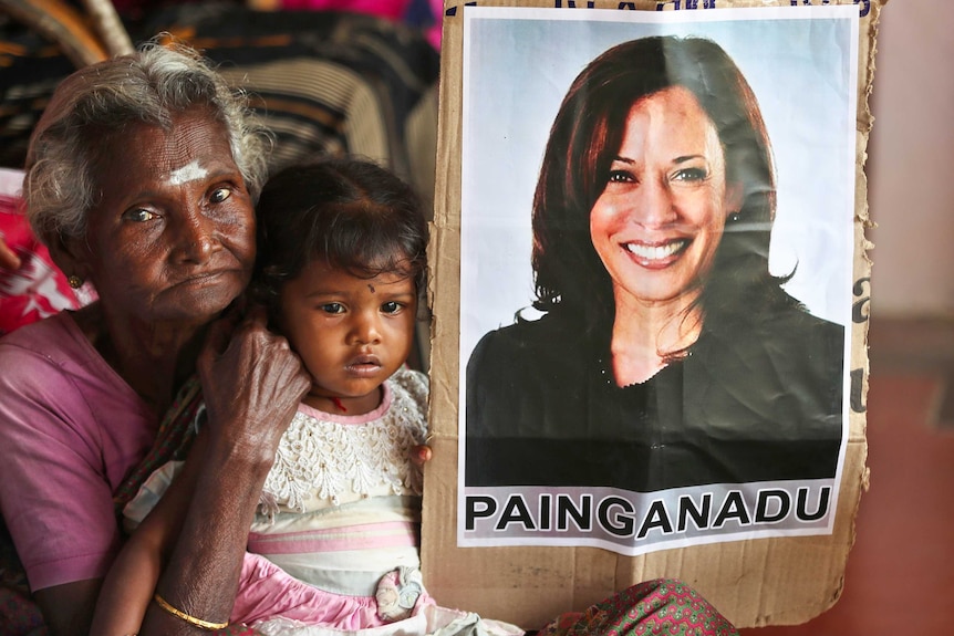 An older Indian woman with a child on her lap holding a poster of Kamala Harris