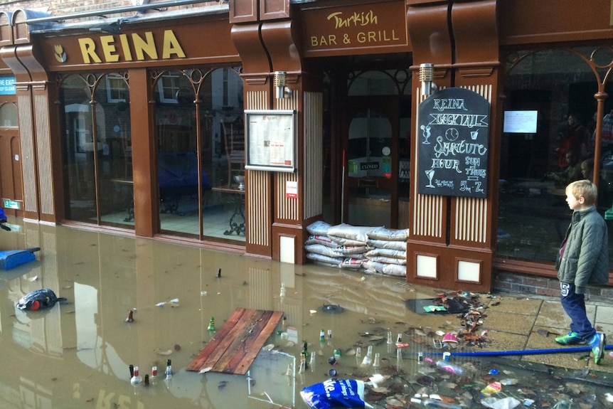 A young boy looks at floodwaters littered with bottles and lapping at the door of a business in the English city of York.