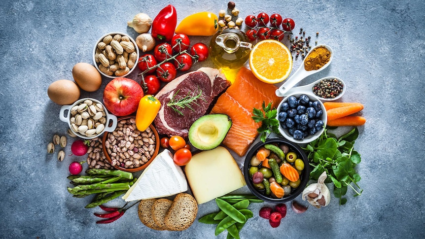 Top view of grey table filled with different types of food including meat, fish, fruits, vegetables, cheese, eggs and nuts.