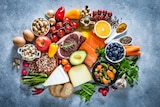 Top view of grey table filled with different types of food including meat, fish, fruits, vegetables, cheese, eggs and nuts.