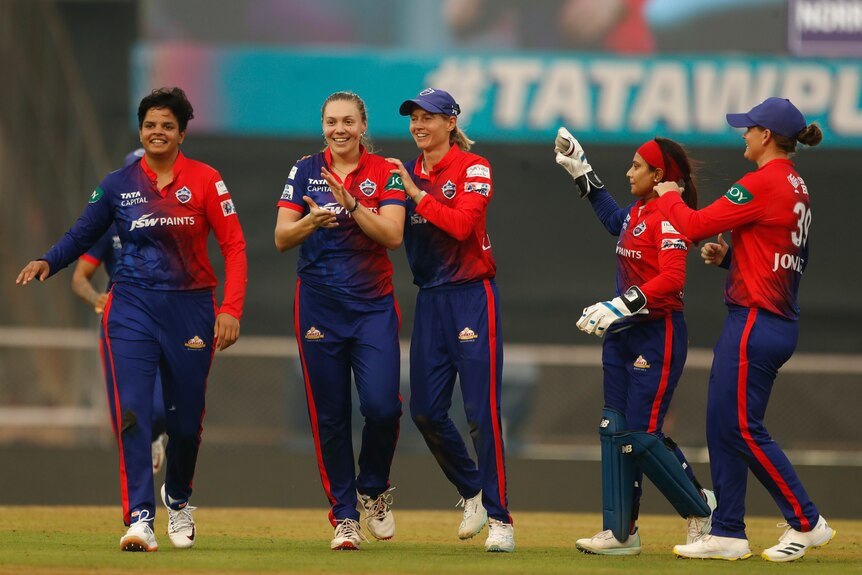 Tara Norris is congratulated by her teammates on the cricket pitch.