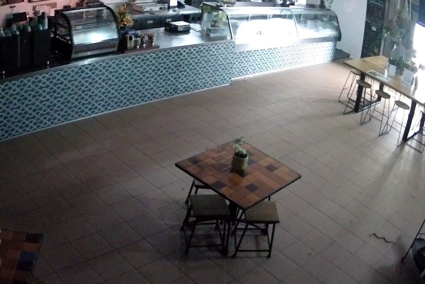 Empty restaurant with a couple of vacant tables and chairs, and a small snake on the ground in the bottom right corner.