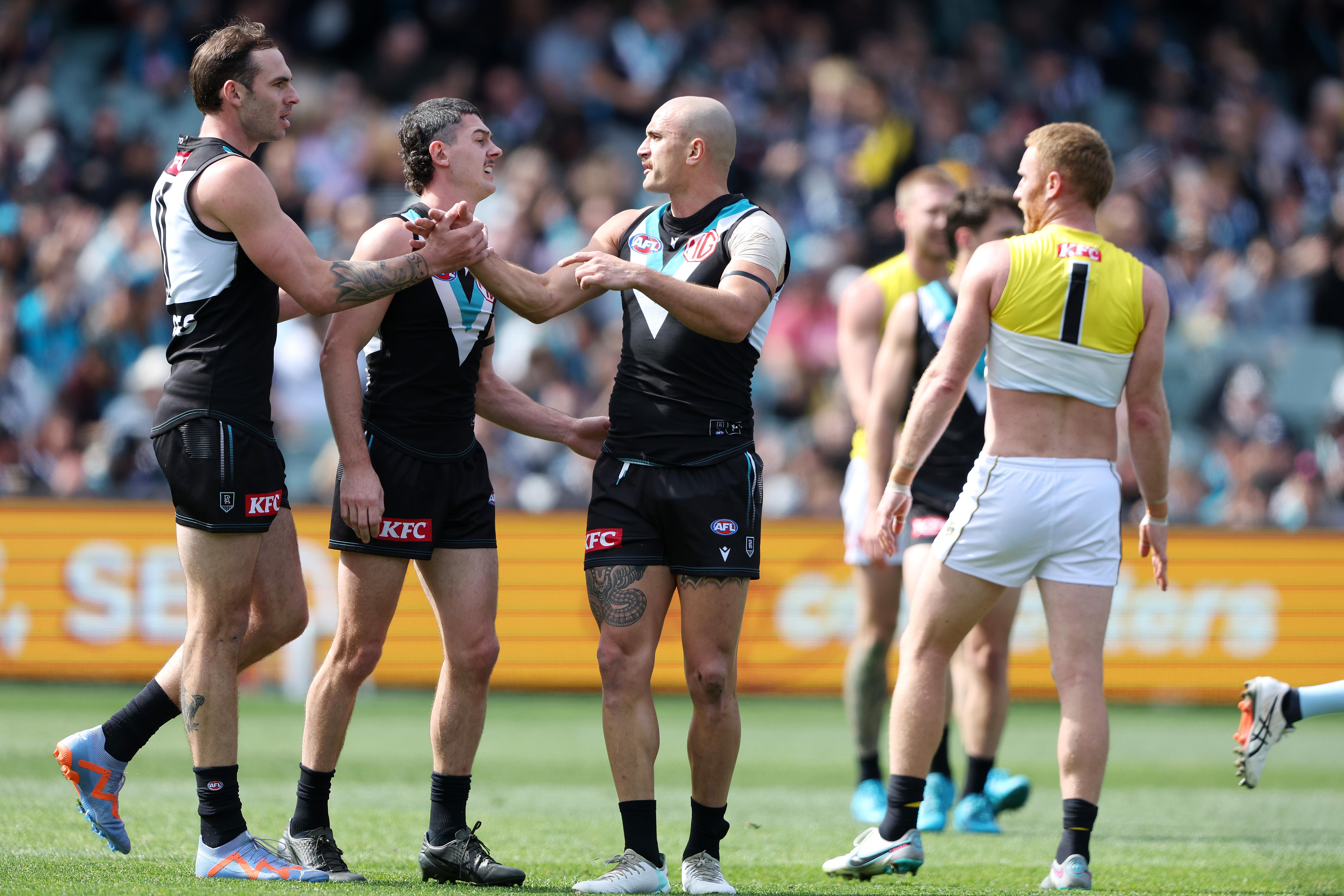 A Port Adelaide AFL player clasps hands with a teammate after kicking a goal.