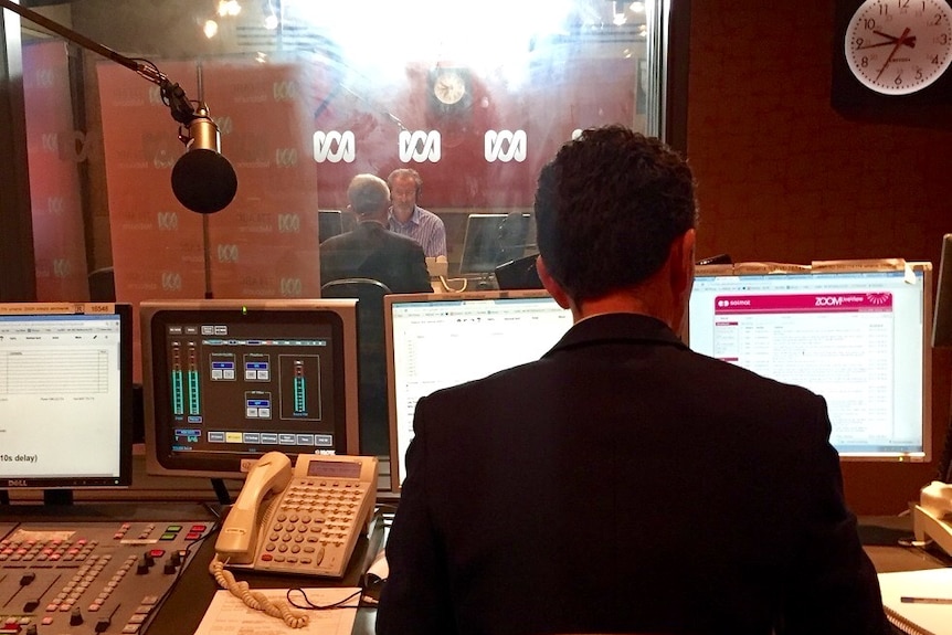 Back of Ziffer in front of computers with Faine in background in studio through window.