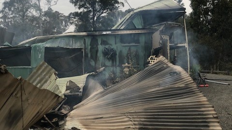 A fence fallen to the right and the charred, smoky remains on a house.