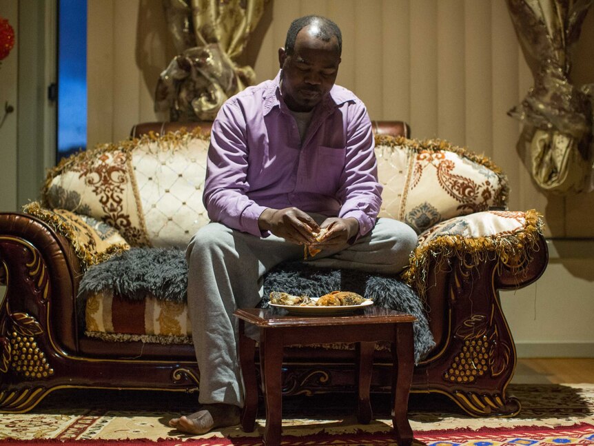 Youssif sits on a lavish African-style couch and picks up the fried fish that his wife Kadiga has prepared.