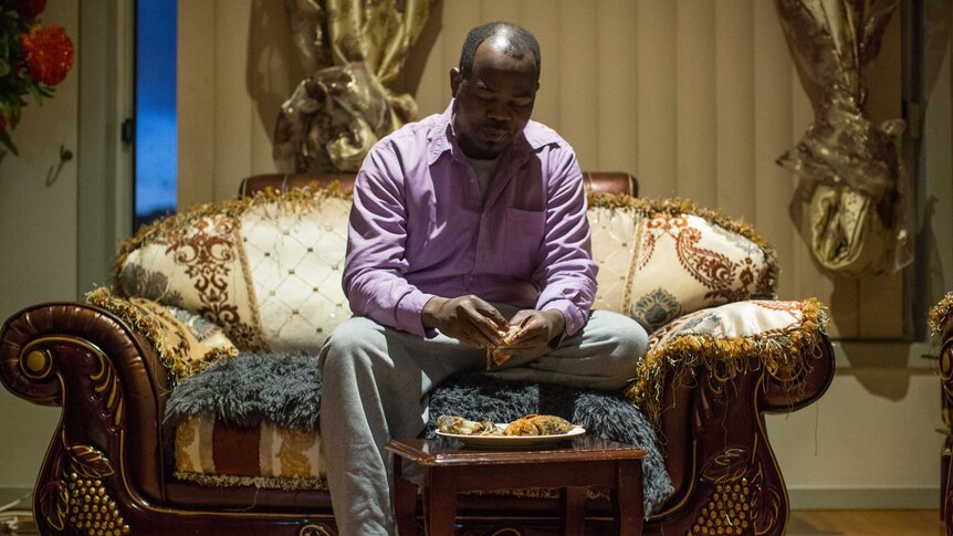 Youssif sits on a lavish African-style couch and picks up the fried fish that his wife Kadiga has prepared.
