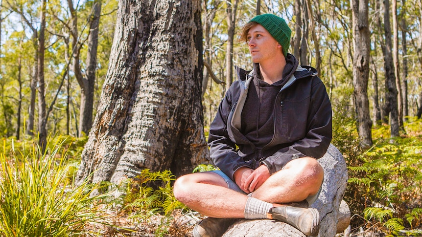 Jamie Graham-Blair sits cross legged in a black peppermint gum forest