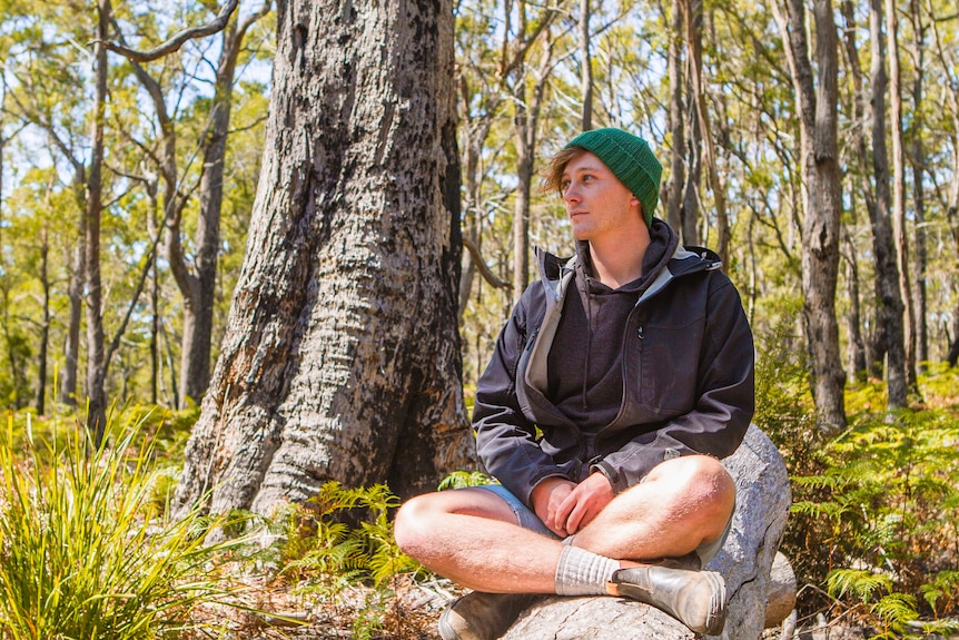 Jamie Graham-Blair sits cross legged in a black peppermint gum forest