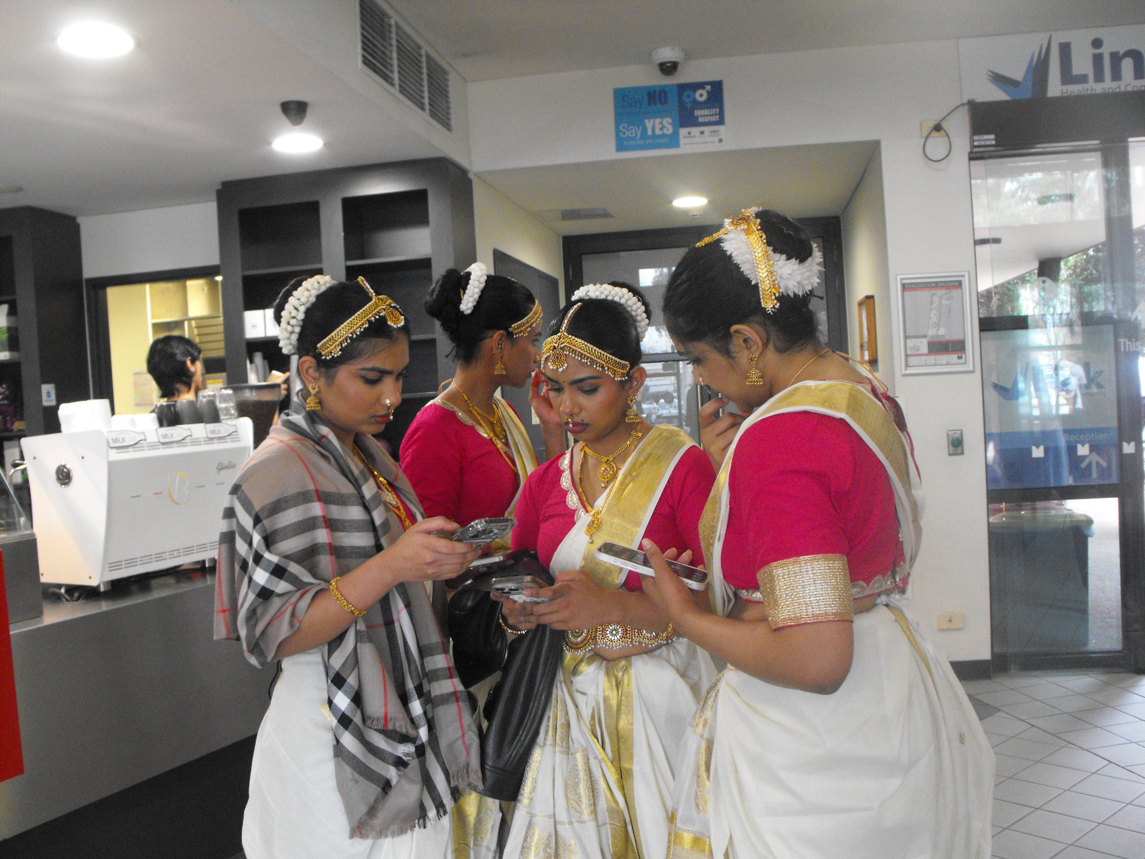 Indian classical dancers in white and gold sarees, flowers in hair, young girls, on phone.