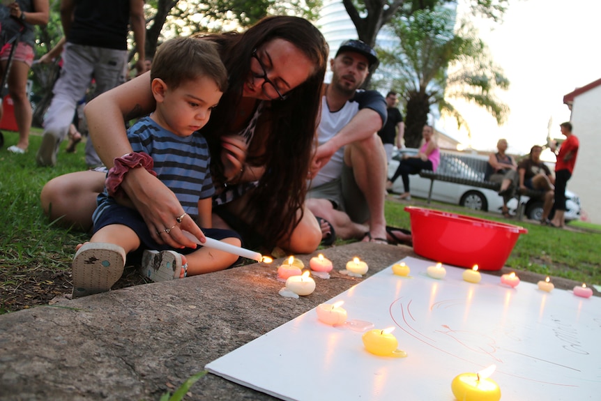 Toddler and mother light candle in park