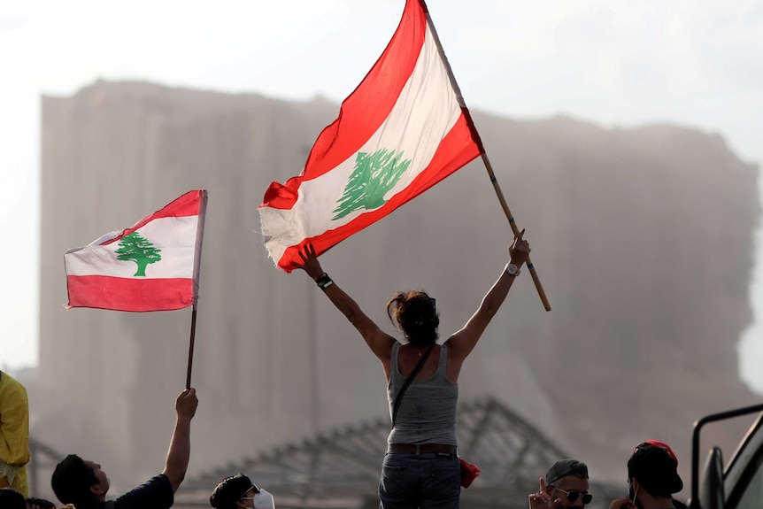 A woman with a Lebanese flag waves it in front of the destroyed port in Beirut