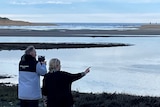 An older tourist takes photos, while another person points at the bird life in the distance.