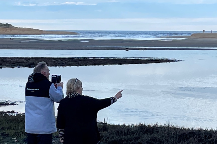 An older tourist takes photos of the lake opening, his partner points  at the bird life in the distance.