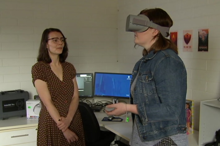 A woman standing using a virtual reality headset while another woman watches
