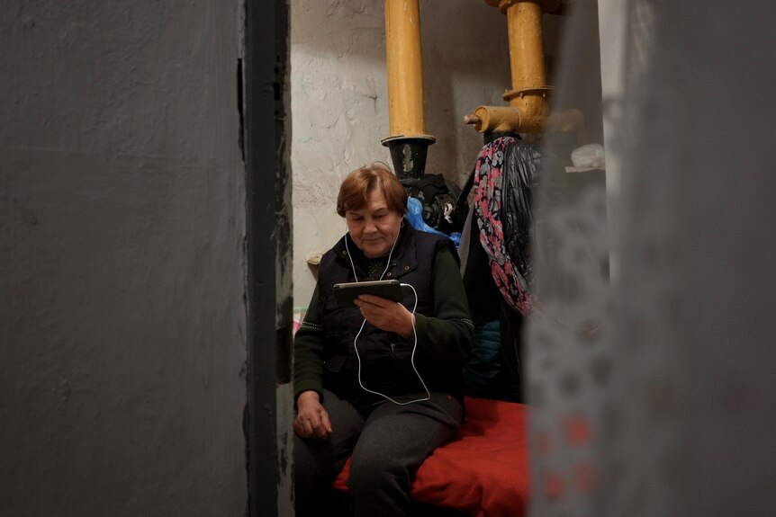 A woman sits on a bed looking at a mobile phone. 