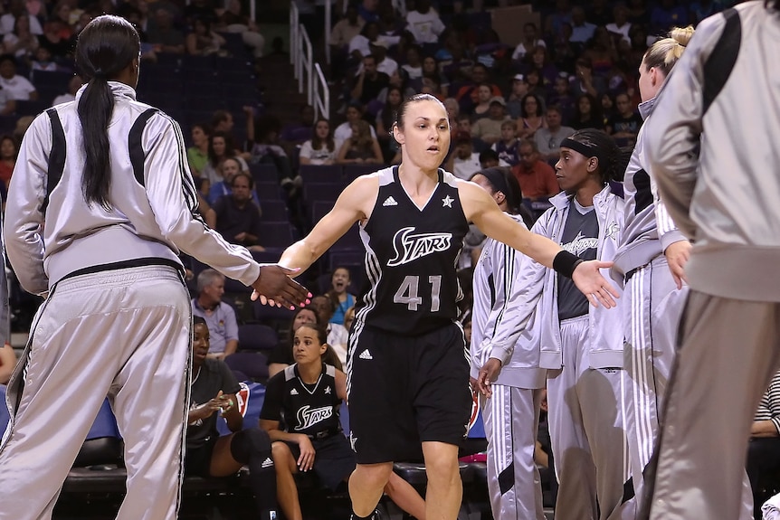 Tully Bevilaqua runs onto the baskteball court through her teammates who have their hands out to high five.