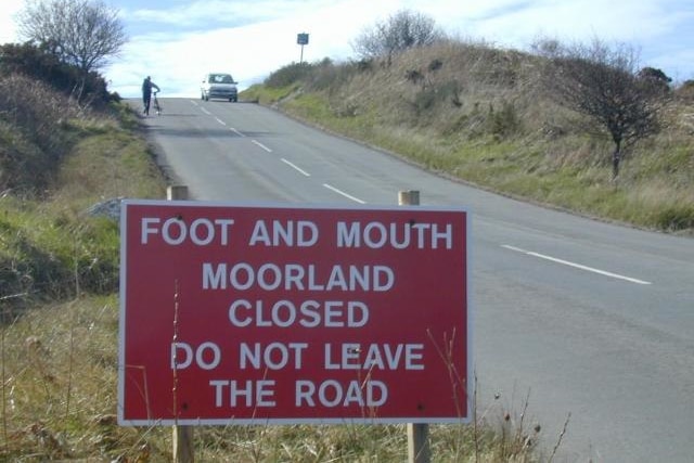 a red sign on a country road reads foot and mouth mooreland close don't leave road
