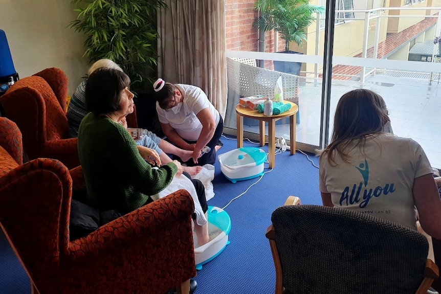 Elderly people sit in chairs and have their feet washed