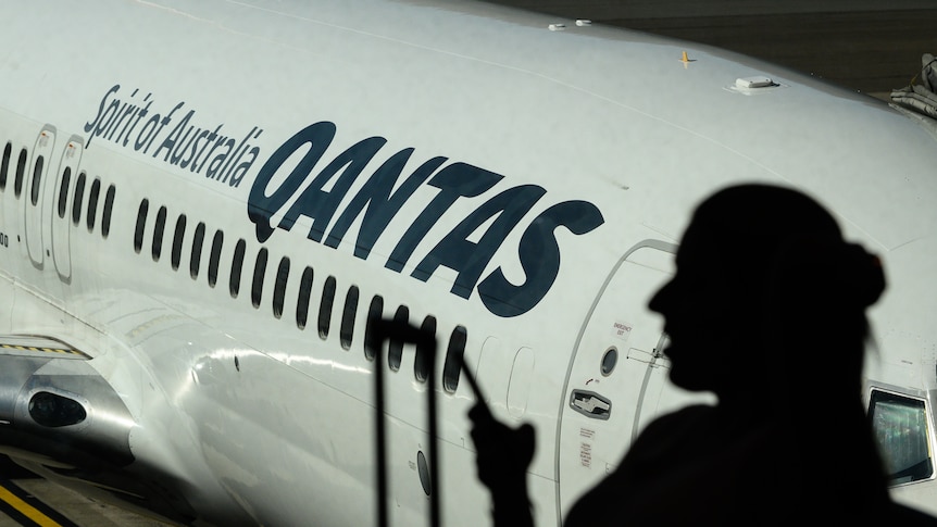 Woman in silhouette stands in front of Qantas plane.