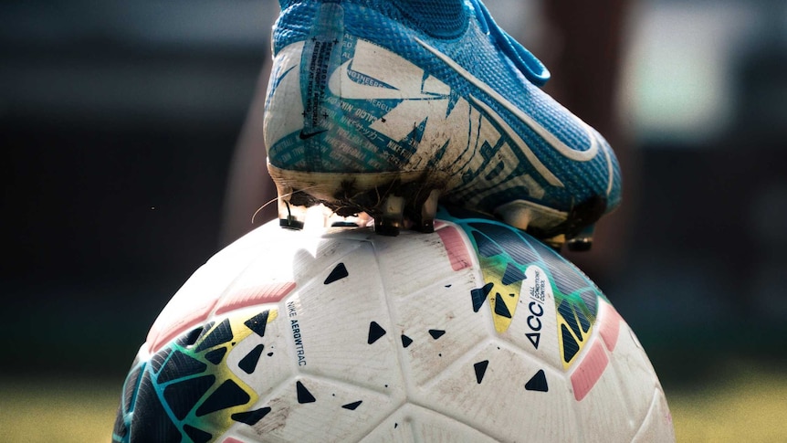 A close up of a foot standing on a soccer ball in a field