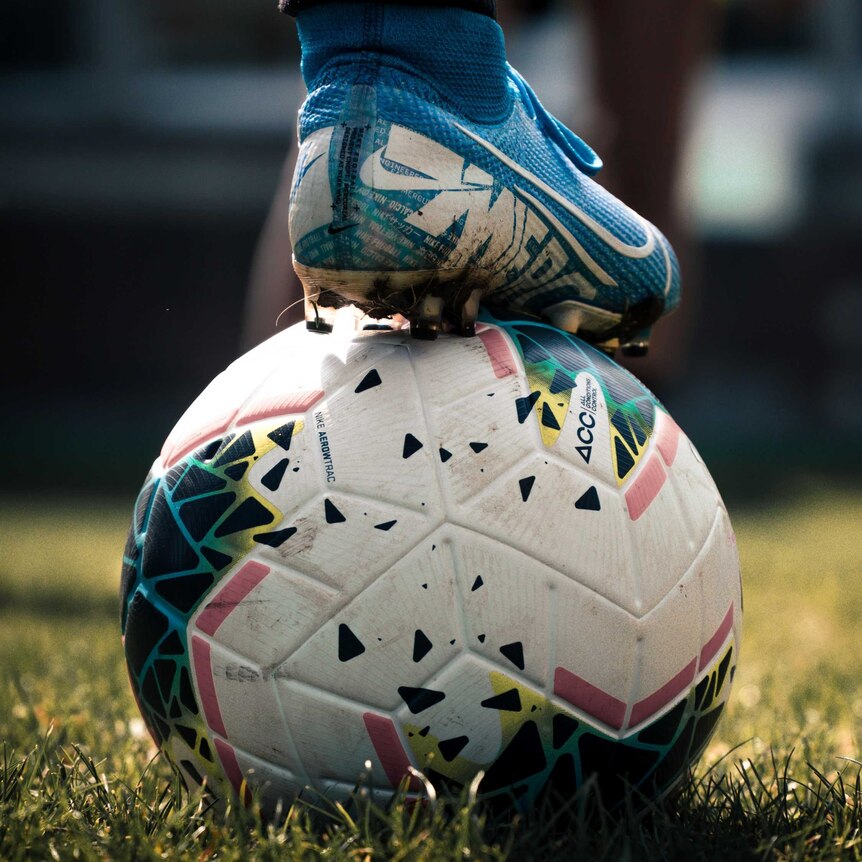 A close up of a foot standing on a soccer ball in a field