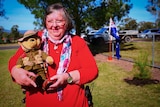 A lady stands holding a bear dressed up as a soldier
