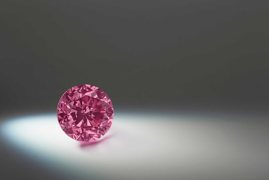 A close up of a vivid pink diamond against a grey backdrop
