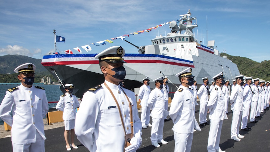 台湾海军人员穿着白色制服，站在一艘新船前。