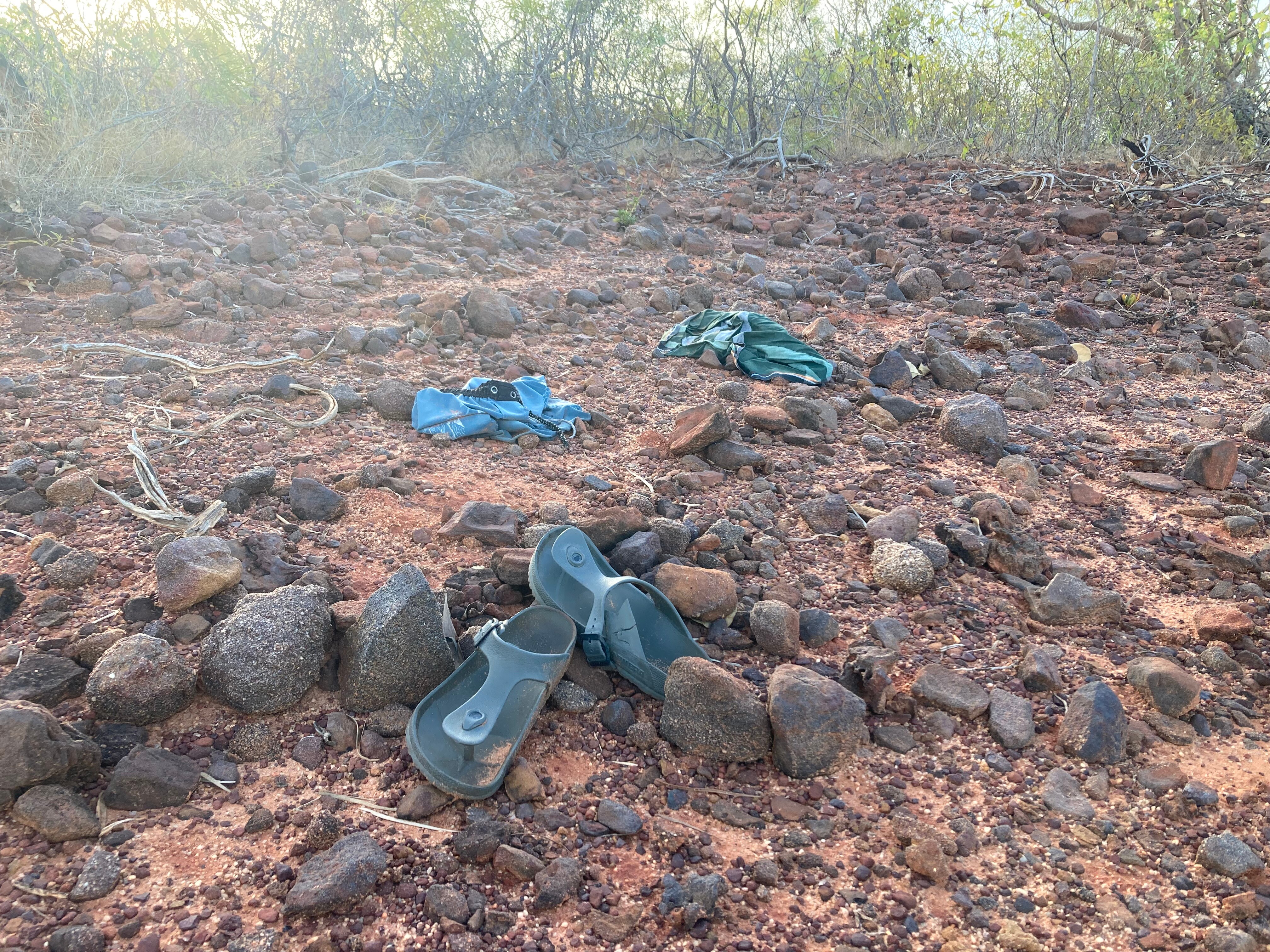 A pair of shoes and some items of clothing left behind on a rocky landscape. 