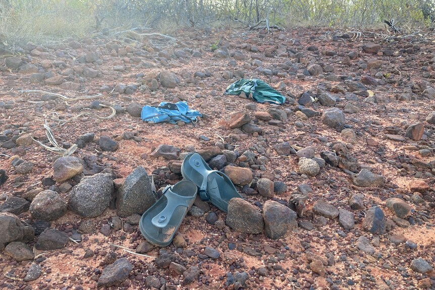 A pair of shoes and some items of clothing left behind on a rocky landscape. 