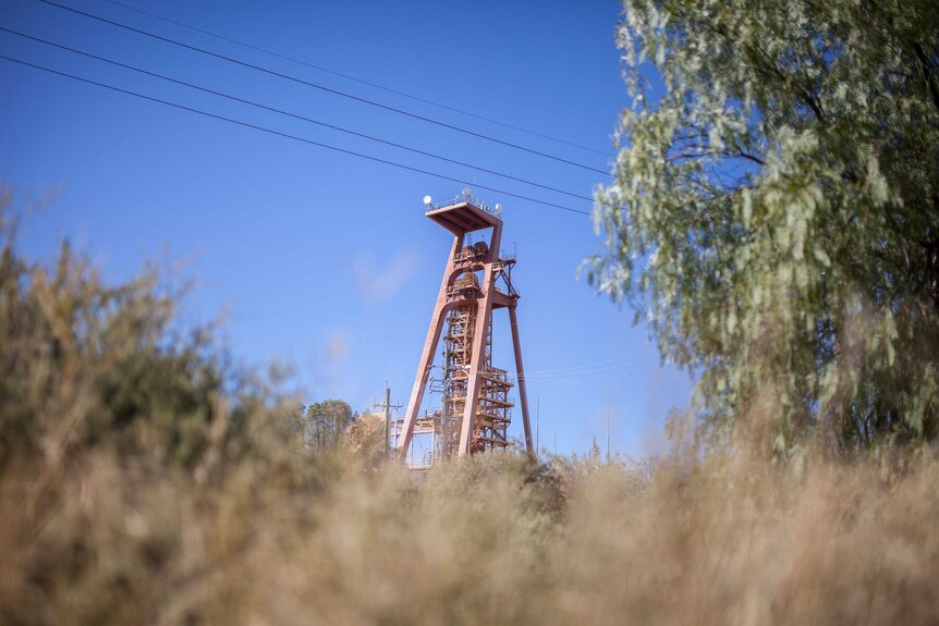 A metal mining shaft rises above the dry dirt and grass like a tower into the blue sky