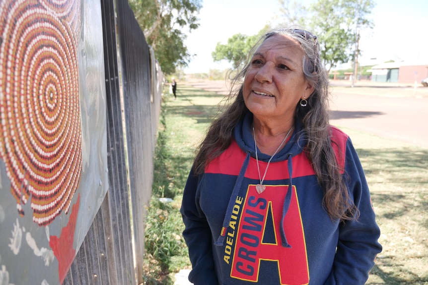 An Indigenous woman looks at Indigenous art painted on a car bonnet