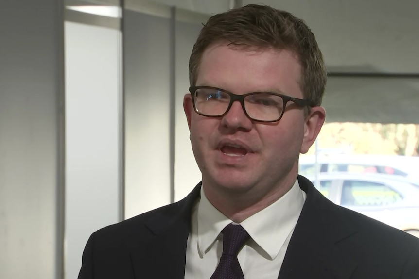 A man standing in a suit with glasses on 