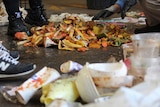 People standing around a pile of food waste, including many fruit skins.