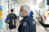 A police officer wearing a mask standing under a covered walkway near a bus